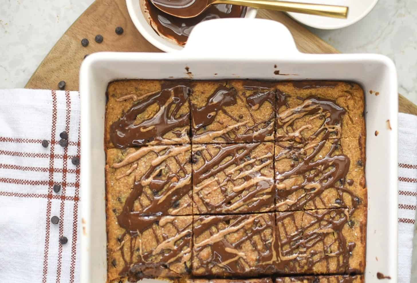 white pan with healthy pumpkin blondies with drizzled chocolate and almond butter on top
