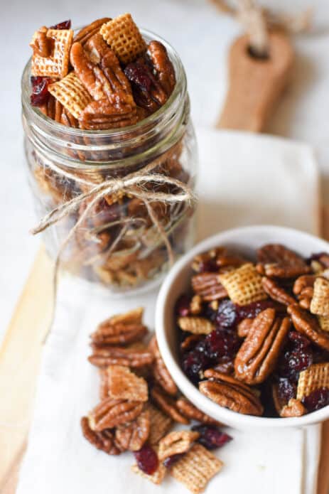 small white bowl and clear mason jar with pecan, cranberry, and chex mix inside of them